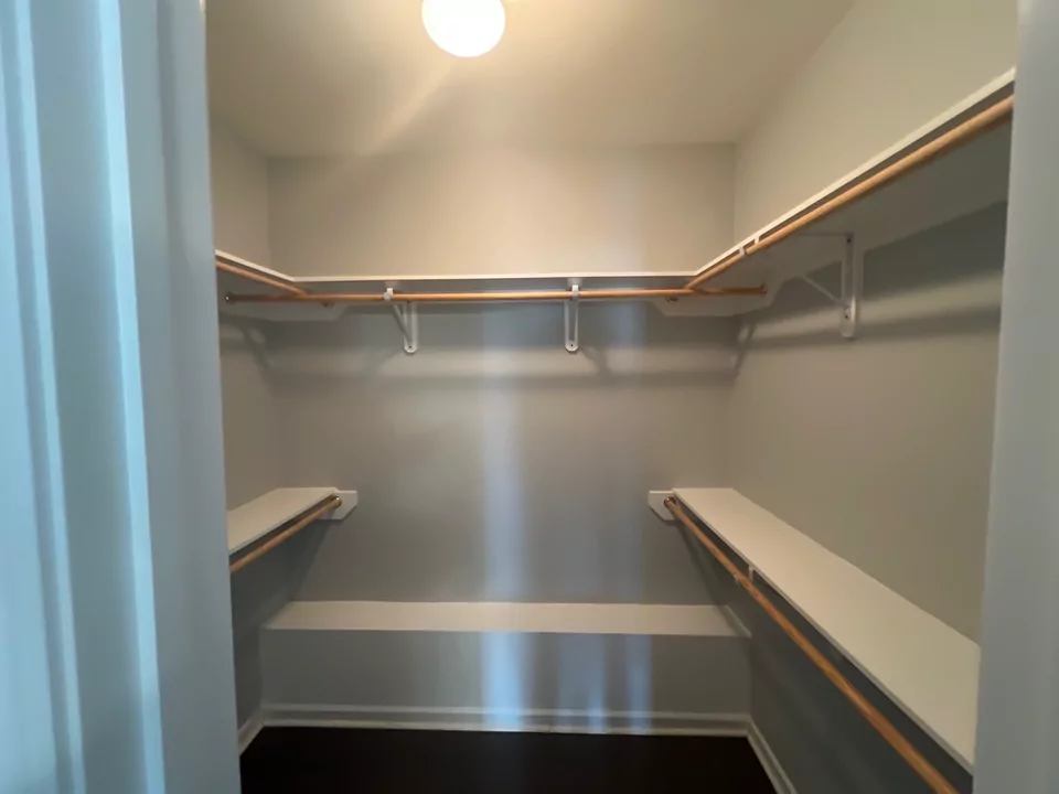 A walk-in closet fitted out with wood-topped shelving and hanging rods on three walls.