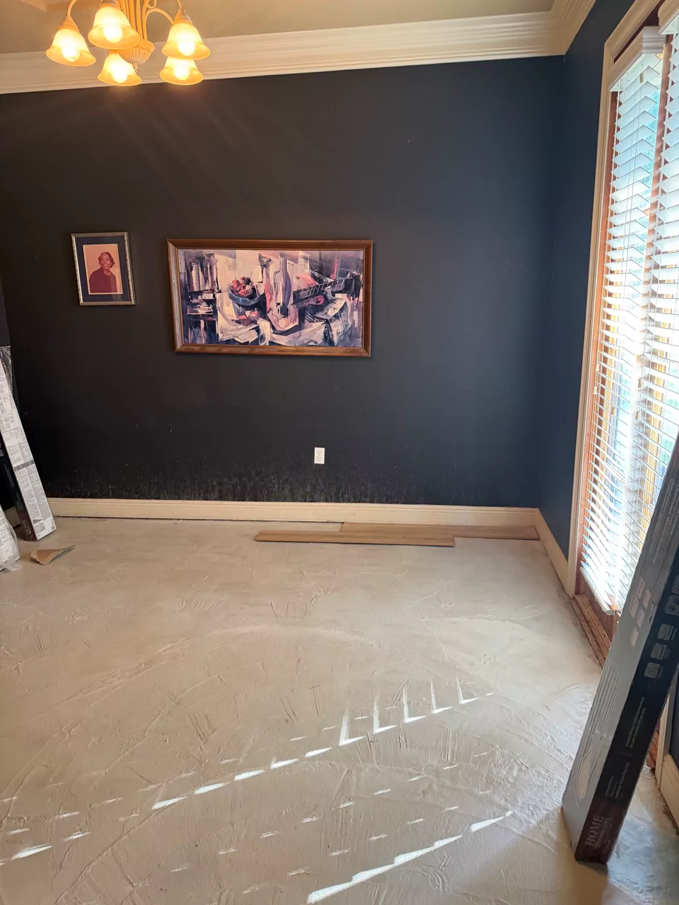 A dining room with deep navy walls and crown molding, still carpeted, with the first boards of the new floor laid out across it.