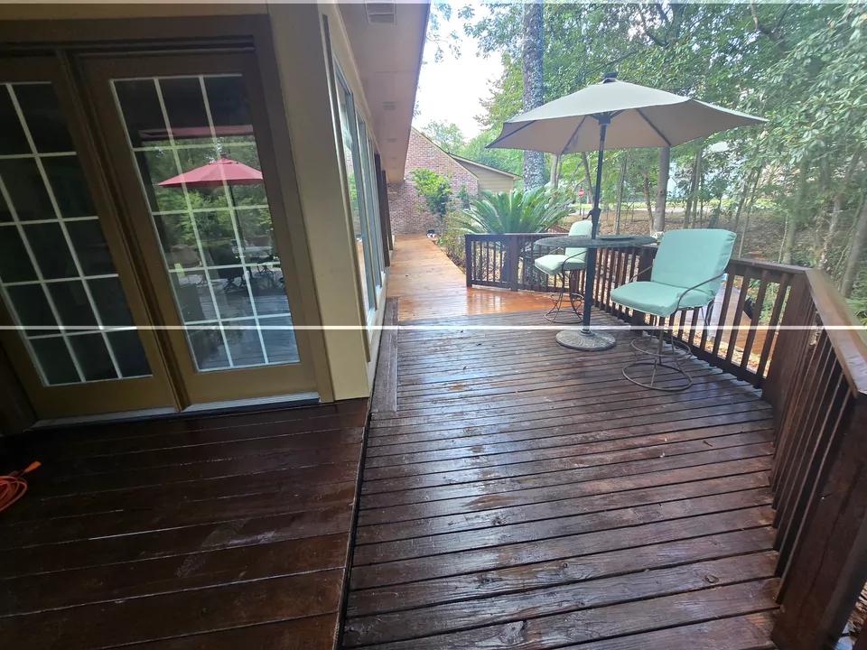 A freshly stained wooden deck off a set of French doors, with a patio umbrella, cushioned chairs and planted beds beyond the rail.